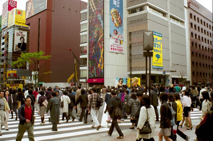 A crossing with some people on it, in Ginza (Tokyo). On the other side of the crossing, there is the Sony building, where playstation 2 were demoed, and the Maxim's restaurant.
